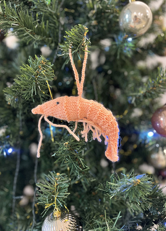 Knitted prawn Christmas ornament hanging on a decorated tree with baubles and lights.
