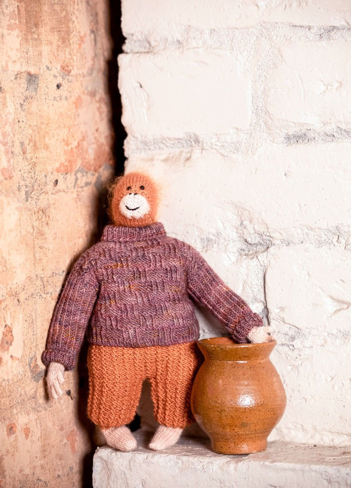 Henri the Orangutan: knitted orangutan in a purple sweater and orange pants, posed beside a small clay pot.