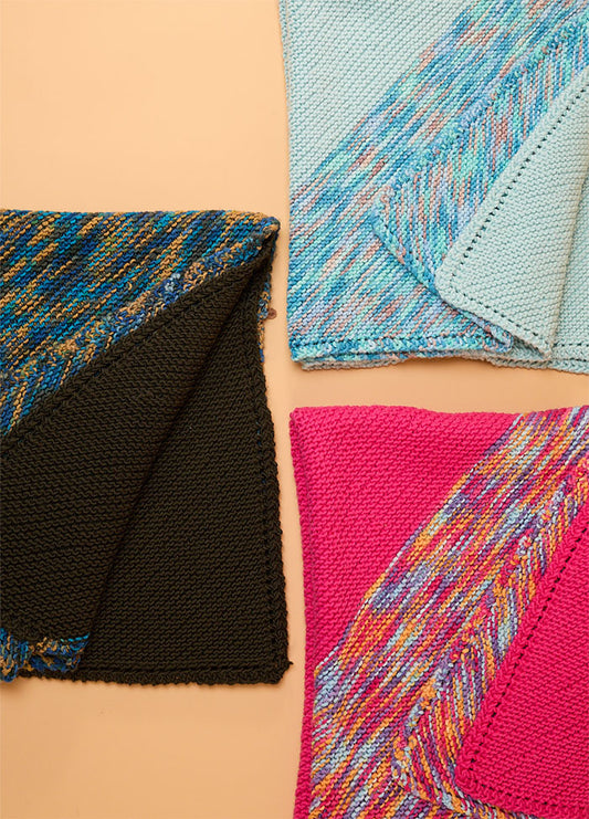 Three Florence Blankets: light blue with multicolored trim, bright pink with patterned edge, and black with a bold multicolored side.