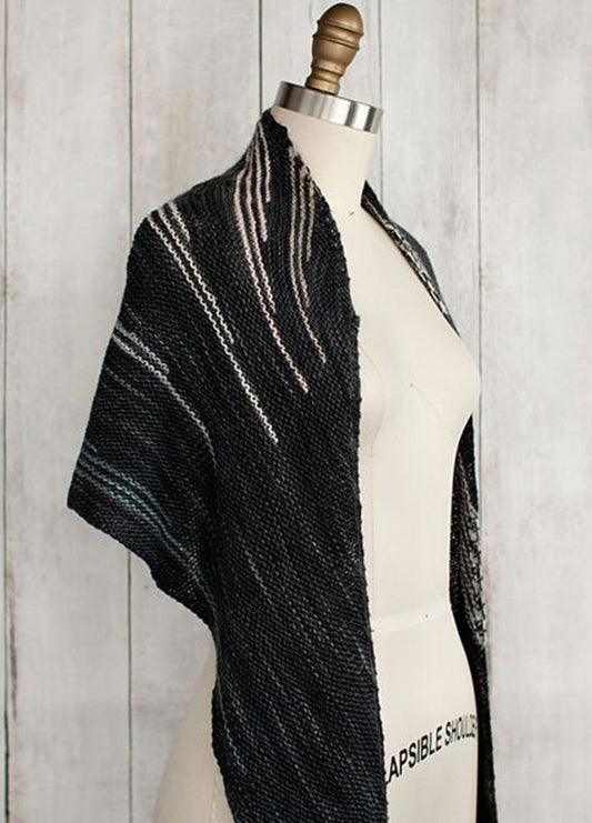 Incremento Shawl draped on a mannequin, featuring dark tones with subtle lighter stripes, shown against a wooden background.
