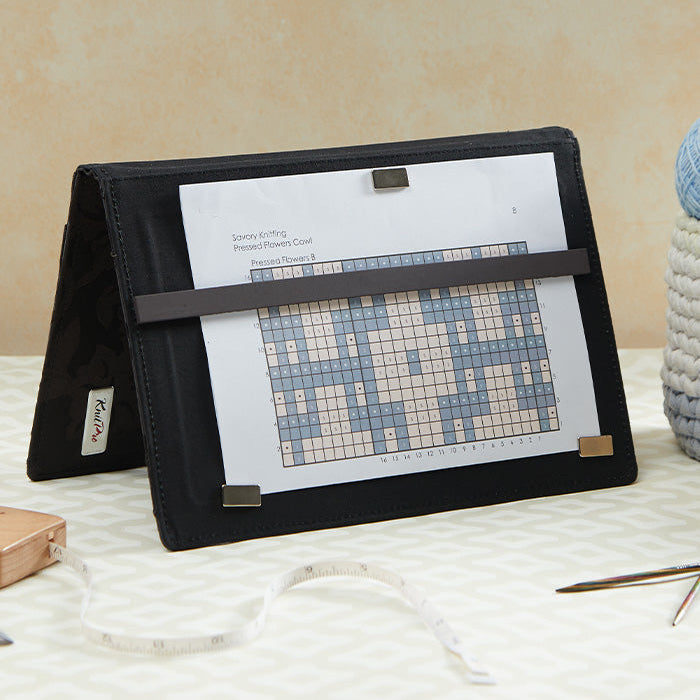 A crafting table features a magma chart keeper, a cross stitch kit, and a book, highlighting essential tools for crafters.