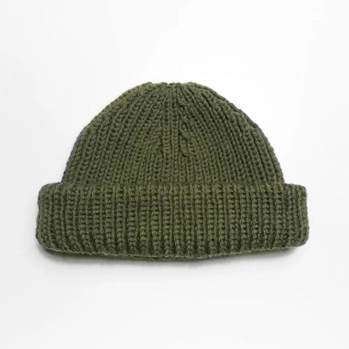 A green knitted beanie with a thick, folded brim is centered on a plain white background, conveying a simple, cozy, and minimalist feel.