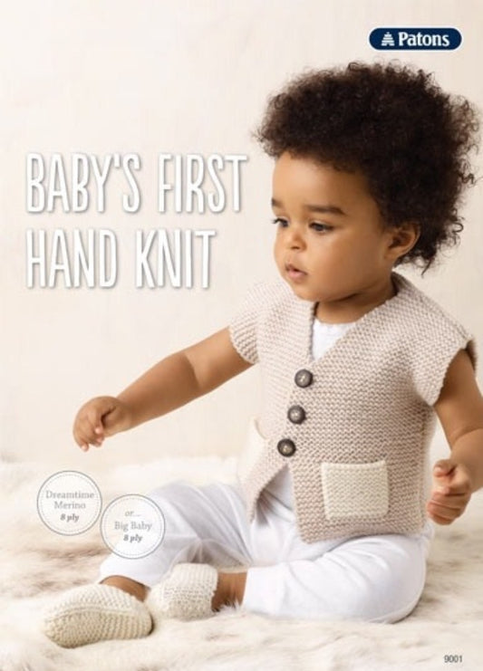 A baby in a cozy beige knit vest with buttons sits on a soft faux fur rug, wearing white pants and knitted slippers. The text reads "Baby's First Hand Knit."