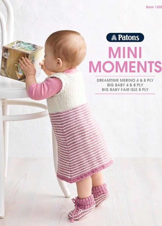 A baby in a white and pink knitted dress stands on a wooden floor, leaning on a white chair. Text says "Patons Mini Moments." The scene feels warm and cozy.