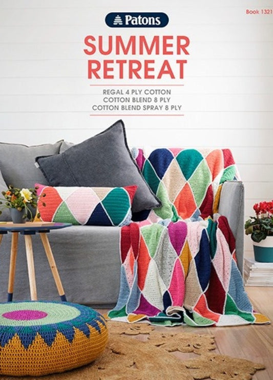 Cozy living room with a colorful patchwork blanket draped over a gray armchair. A matching cushion, plants, and yarn pouf add to the cheerful vibe.