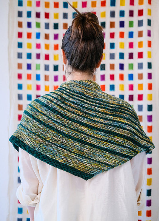 Striped Saturn Shawl in green, yellow, and blue, worn over shoulders, with a colorful grid background.