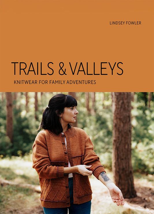 Person wearing an orange knitted sweater in a forested setting, cover of Lindsey Fowler’s knitwear book.