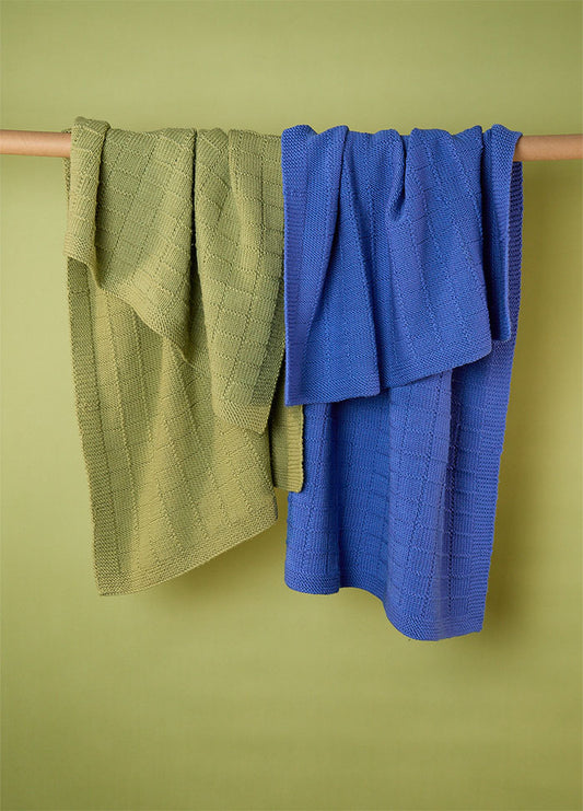 Two Window Pane Blankets in green and blue, hanging on a wooden rod, each featuring a textured square panel design.