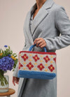 A woman holds a colorful knitted bag adorned with flowers, showcasing her unique style and love for handmade accessories.
