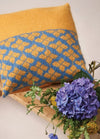 A knitted cushion featuring a pattern of blue and yellow flowers on a textured background.