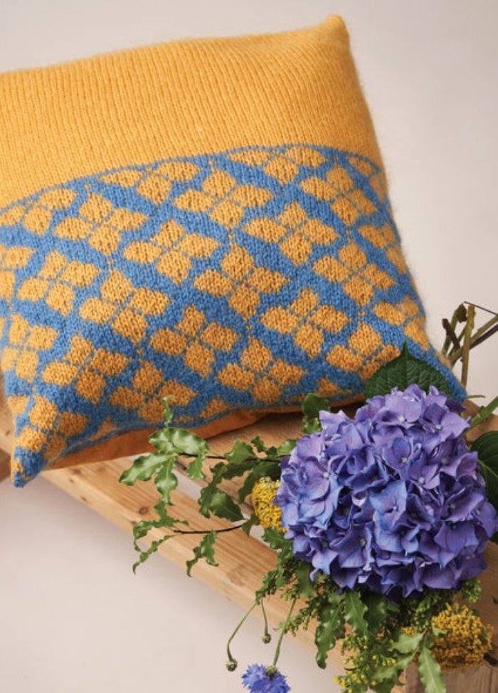 A knitted cushion featuring a pattern of blue and yellow flowers on a textured background.