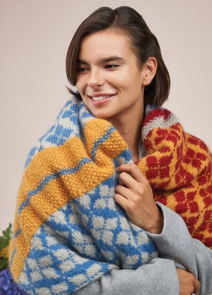 A woman models a stylish knitted scarf, highlighting its intricate design and vibrant color.