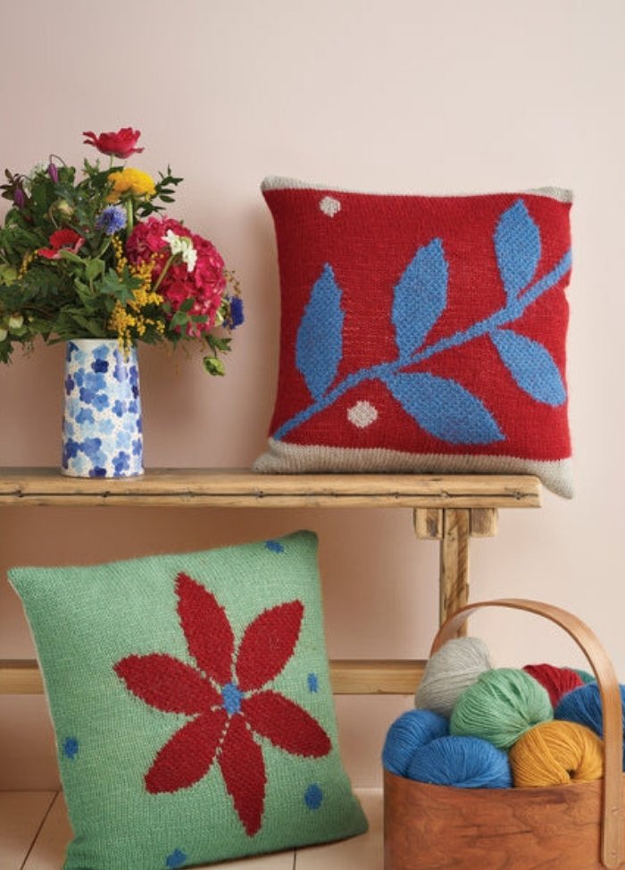 Two decorative pillows featuring vibrant patterns and colorful yarn accents arranged on a soft surface.