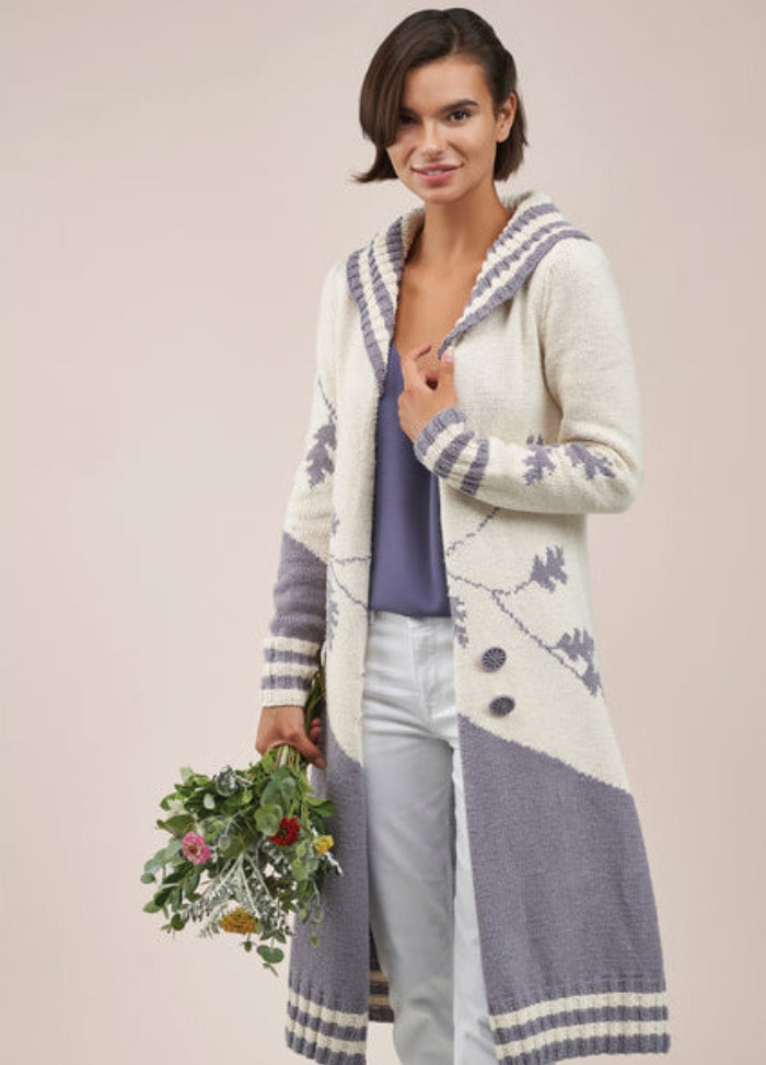Woman smiling, wearing a long cream and gray hooded cardigan with a nature pattern, holding a bouquet of flowers. Tone is warm and inviting.