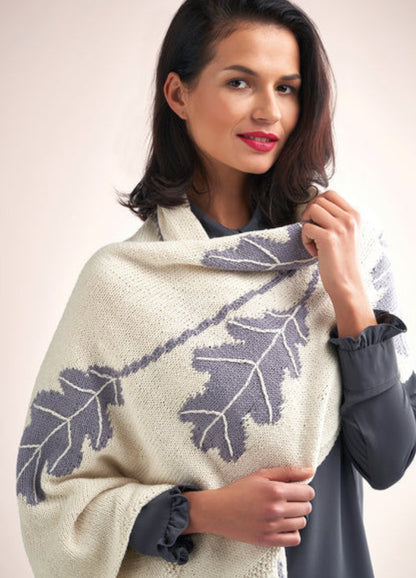 Woman draped in a cream shawl with large gray leaf patterns, wearing a dark top. She has shoulder-length hair, subtle smile, and red lipstick. Elegant and serene.