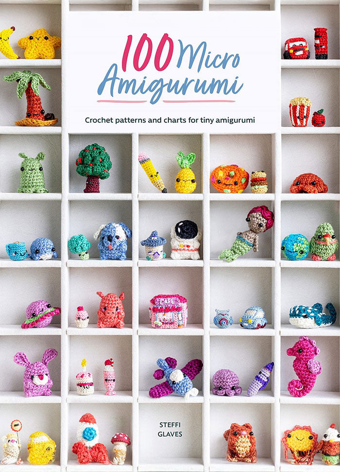 Cover of 100 Micro Amigurumi, showing a display of tiny crocheted figures—like animals, fruits, and mythical creatures—arranged in a white cubby-style shelving unit, with the title in playful blue and pink lettering above.