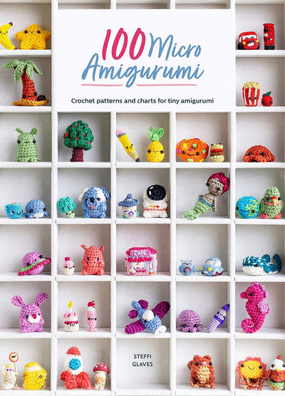 Cover of 100 Micro Amigurumi, showing a display of tiny crocheted figures—like animals, fruits, and mythical creatures—arranged in a white cubby-style shelving unit, with the title in playful blue and pink lettering above.