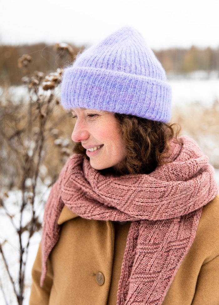 Hazy Hat: light purple knitted hat worn with a pink textured scarf and tan coat in a wintry outdoor setting.