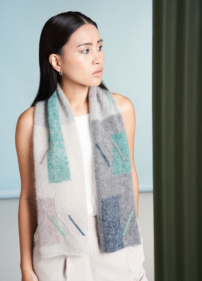 A person with long dark hair, wearing a white top and patterned scarf, gazes to the side against a soft blue and green background. The mood is calm and thoughtful.