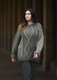 Woman in a cozy, oversized gray knit sweater walks confidently in an urban setting. The sweater features intricate cable patterns, conveying warmth.