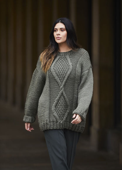 Woman in a cozy, oversized gray knit sweater walks confidently in an urban setting. The sweater features intricate cable patterns, conveying warmth.