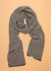 Black and white hand-knitted scarf featuring a classic houndstooth pattern, displayed flat on a beige background – timeless and elegant winter accessory.