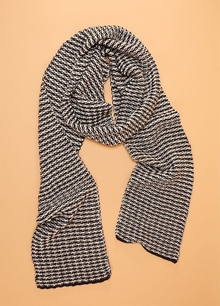 Black and white hand-knitted scarf featuring a classic houndstooth pattern, displayed flat on a beige background – timeless and elegant winter accessory.