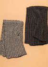 Two hand-knitted scarves displayed on a beige background – one with bold black and white stripes, the other in solid black featuring a textured knit pattern.