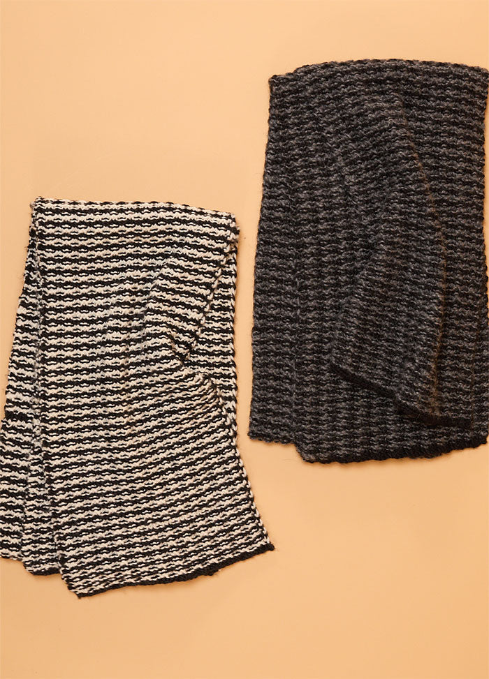 Two hand-knitted scarves displayed on a beige background – one with bold black and white stripes, the other in solid black featuring a textured knit pattern.