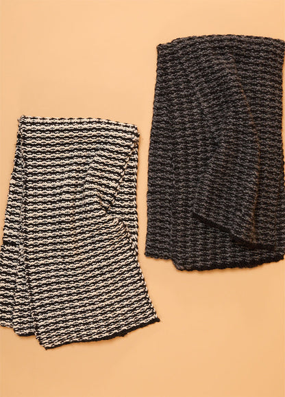 Two hand-knitted scarves displayed on a beige background – one with bold black and white stripes, the other in solid black featuring a textured knit pattern.