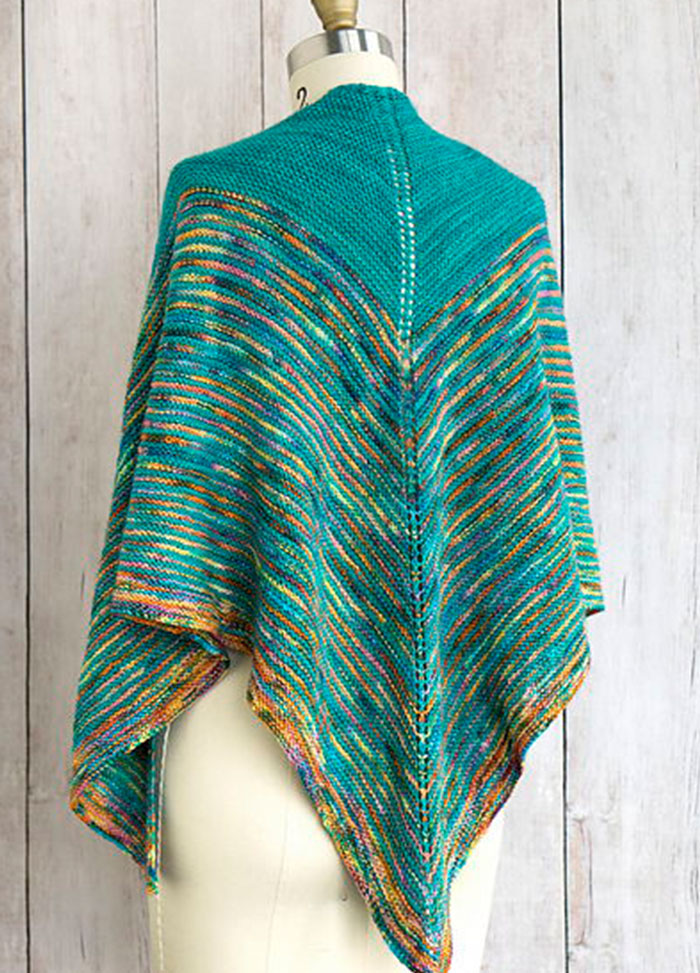 Allspice Shawl draped on a mannequin, featuring a vibrant V-shaped design in teal, orange, yellow, and blue with a curved edge and central spine.