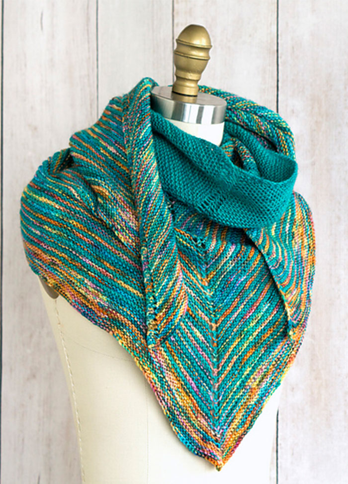 Allspice Shawl on a mannequin, featuring chevron stripes in teal and multicolored yarn with orange, yellow, and green tones, draped stylishly around the shoulders.