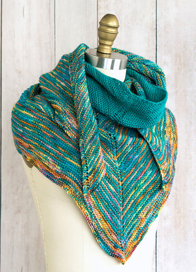 Allspice Shawl on a mannequin, featuring chevron stripes in teal and multicolored yarn with orange, yellow, and green tones, draped stylishly around the shoulders.