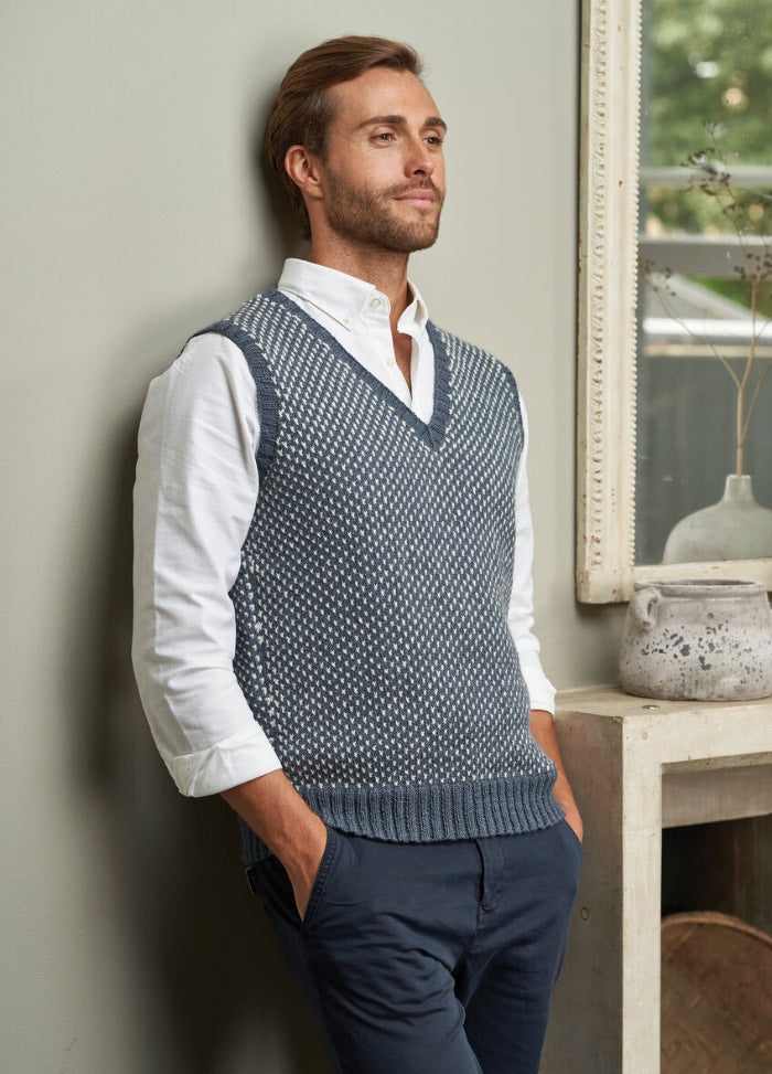 A man in a knitted vest over a white shirt, standing confidently with a neutral expression.