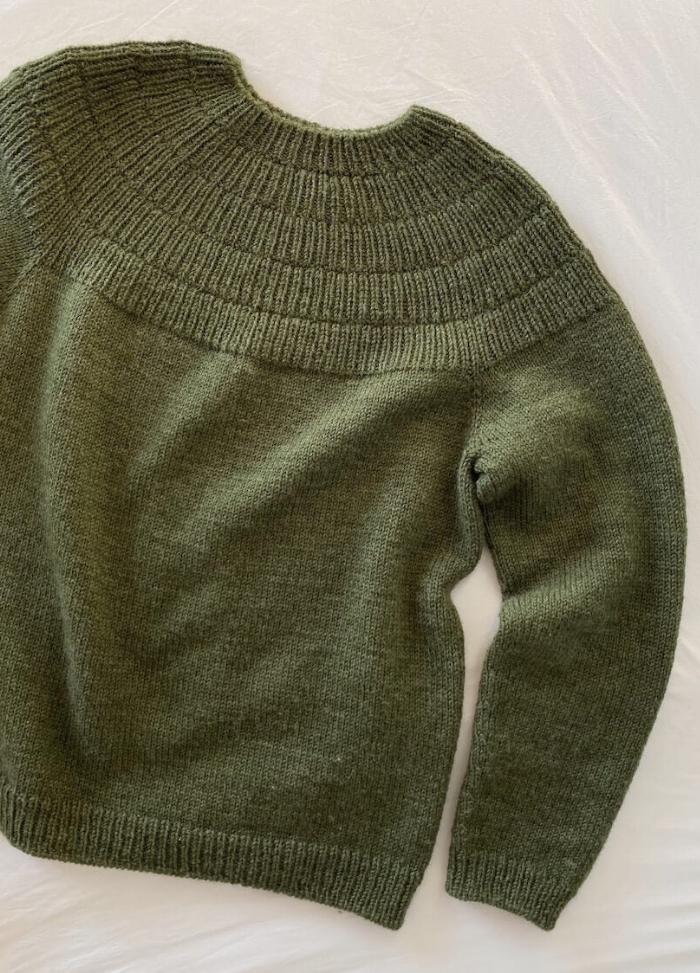 Close-up of a textured olive-green knitted sweater, showcasing intricate ribbed patterns on the yoke against a plain background.