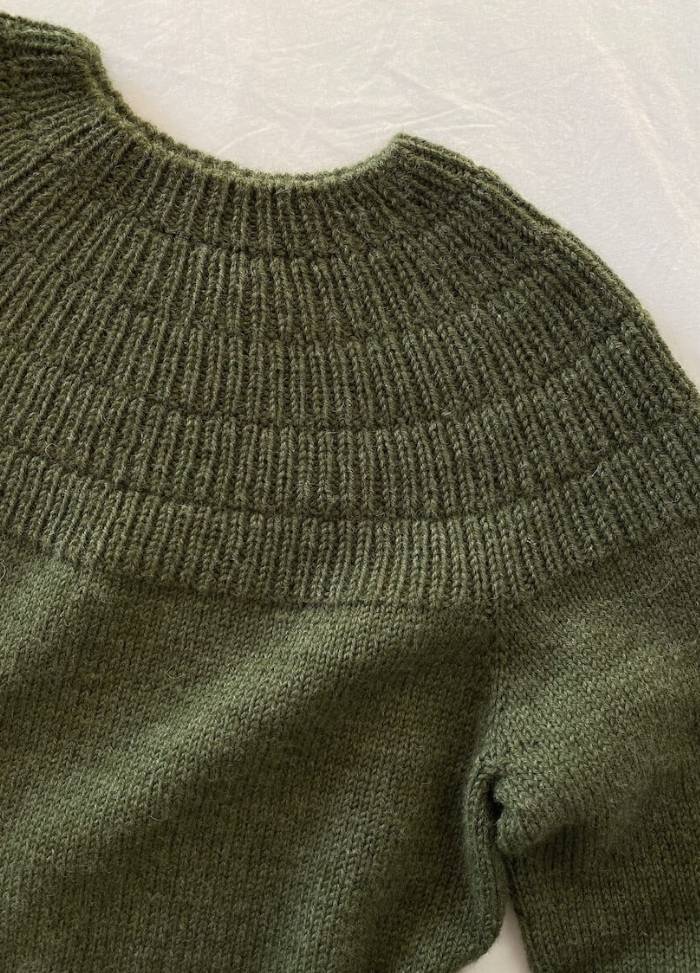 Green wool sweater with a ribbed, circular yoke and cuffs, laid flat on a white surface. The texture appears soft and cozy.