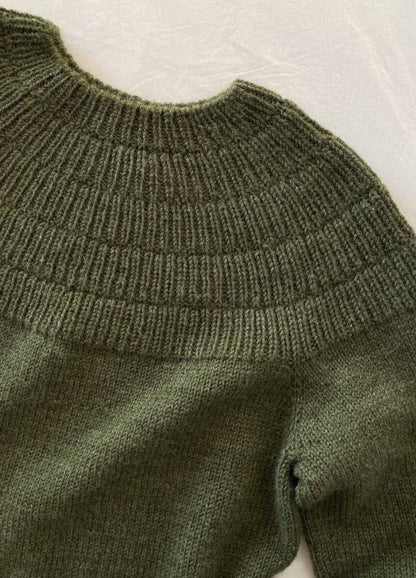 Green wool sweater with a ribbed, circular yoke and cuffs, laid flat on a white surface. The texture appears soft and cozy.