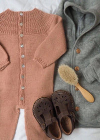 Brown knit baby onesie with buttons, grey hooded coat, brown shoes, and wooden hairbrush. Soft textures evoke warmth and coziness.