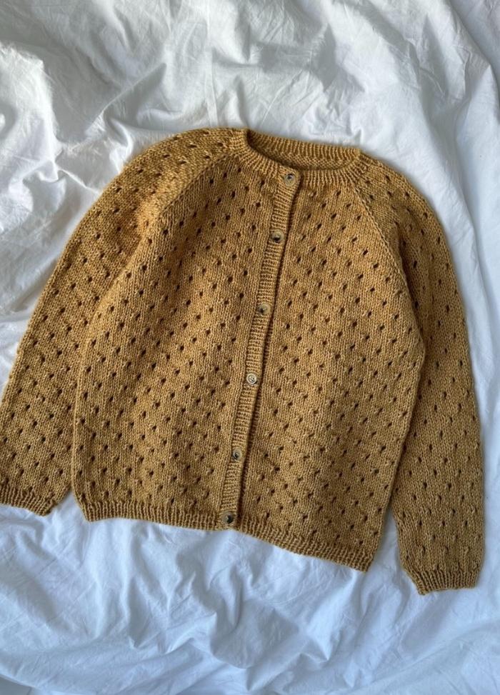 Yellow knitted cardigan with a round neckline and button-up front lies on a white textured blanket. The sweater features a dotted pattern.