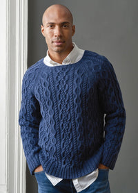 A man dressed in a blue sweater and jeans poses confidently, showcasing a relaxed style.