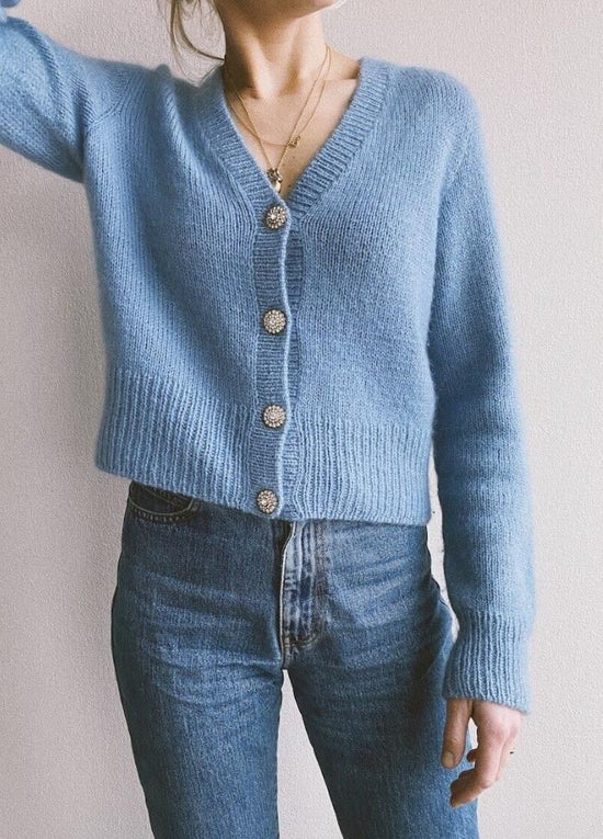 A person wearing a soft blue knit cardigan with decorative buttons and blue jeans. The close-up framing captures a casual, cozy style.