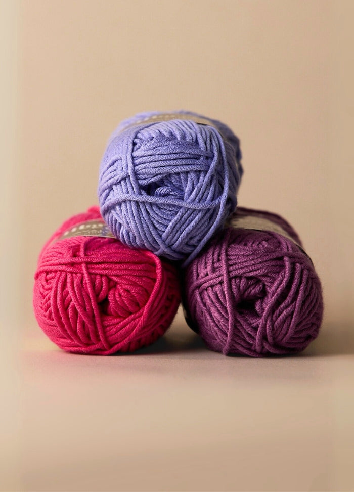 Three balls of soft, matte-finish pima cotton yarn in vibrant colors, ideal for spring and summer knitting and crochet projects.