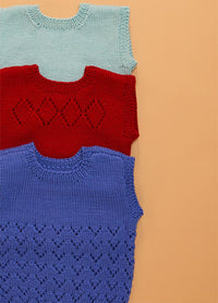 Vertical arrangement of three hand-knitted baby singlets on a peach background – light blue singlet with simple knit texture, red singlet featuring central diamond motif, and purple singlet with wavy stitch pattern along the lower half.