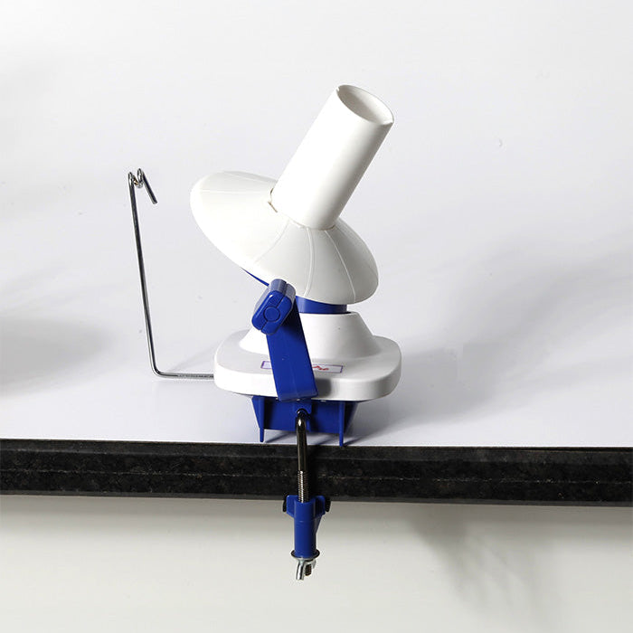 A white and blue hand-operated yarn winder on a table, featuring a clamp for secure use and compact design for easy storage.