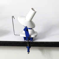 A white and blue hand-operated yarn winder on a table, featuring a clamp for secure use and compact design for easy storage.