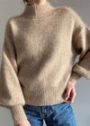 Model wearing a beige Balloon Sweater with high neckline and voluminous sleeves, paired with blue jeans.