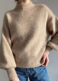 Model wearing a beige Balloon Sweater with high neckline and voluminous sleeves, paired with blue jeans.