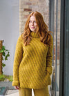 A woman with long auburn hair in a cozy yellow sweater and matching pants stands by a window. She gazes thoughtfully outside, exuding a calm, reflective mood.
