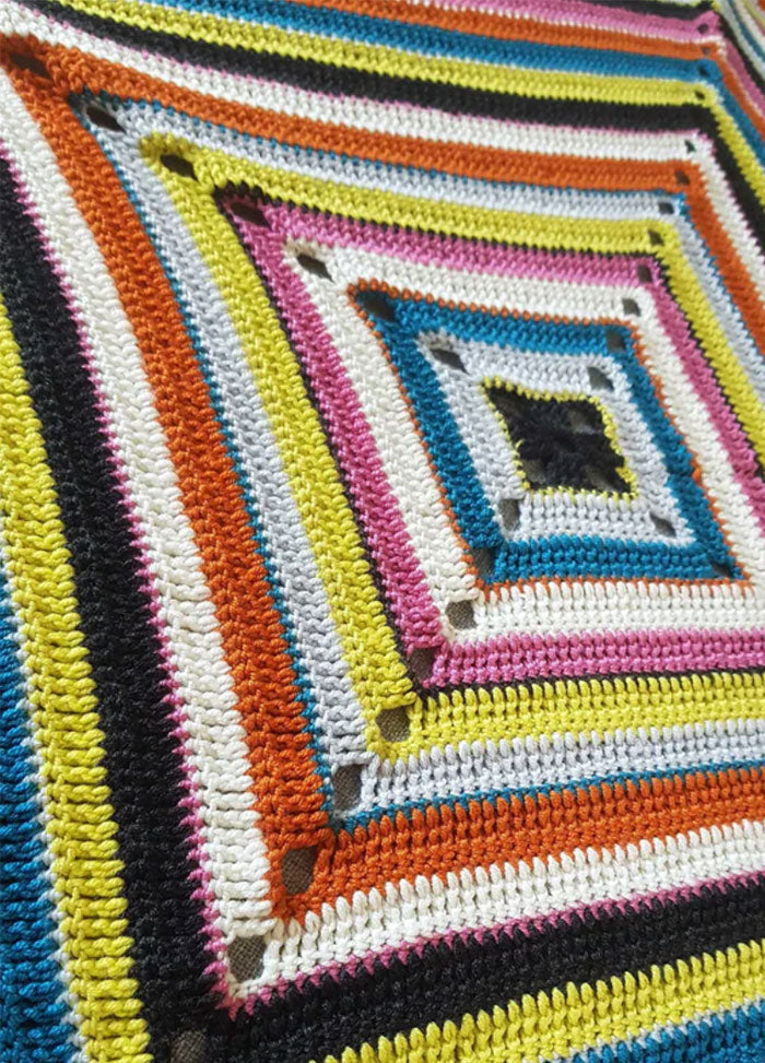 Barcelona Blanket – vibrant crocheted blanket featuring concentric squares in black, white, yellow, orange, pink, blue, and gray; each square bordered with contrasting yarns to create a striking geometric pattern.