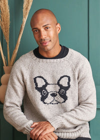 A man in a cozy sweater adorned with a dog graphic, looking cheerful in a natural setting.